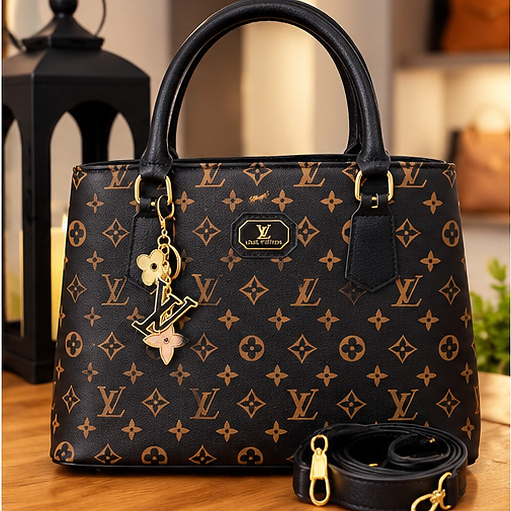 Bolsa tote monograma marrom com acabamento preto, alças curtas, pingente dourado e alça longa removível